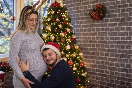 husband hugging pregnant wife's belly in front of a Christmas tree