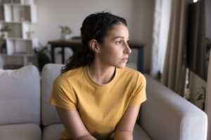 Woman wearing a yellow shirt sitting on a couch looking out a window.